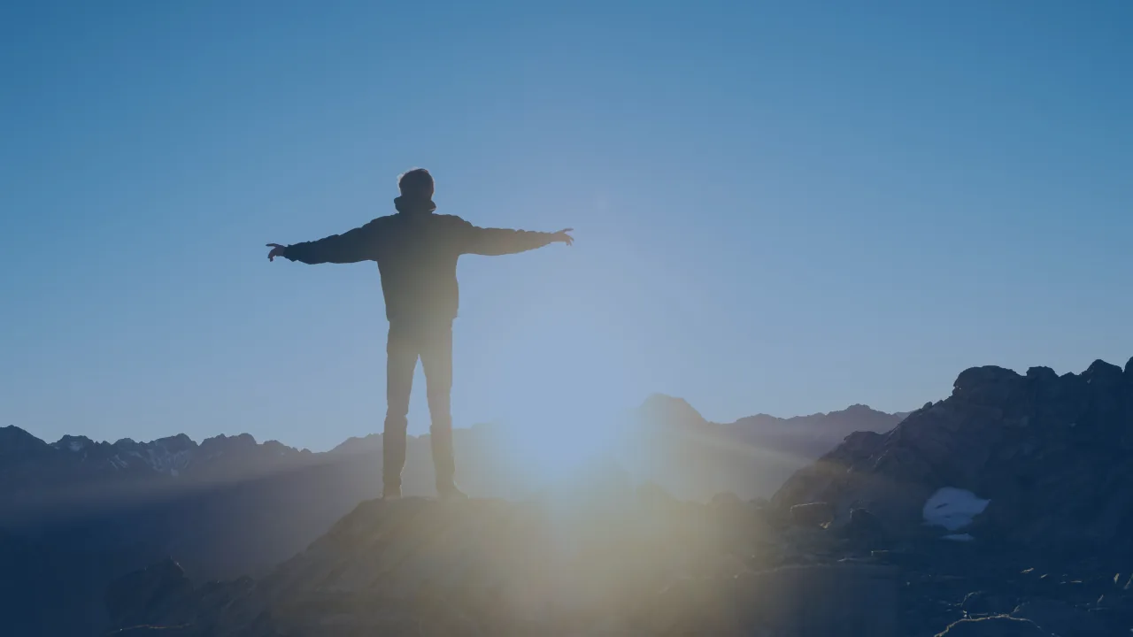 A person with arms open on a ridge at sunrise